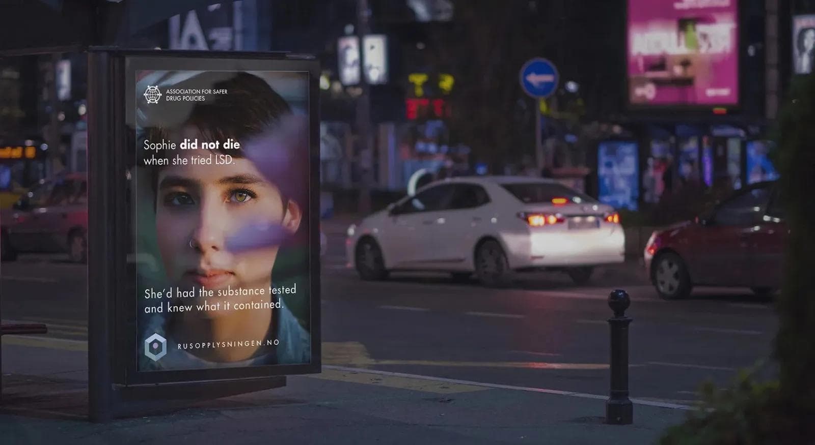 Backlit bus shelter ad at night showing a Rusopplysningen poster — 'Sophie did not die when she tried LSD'.