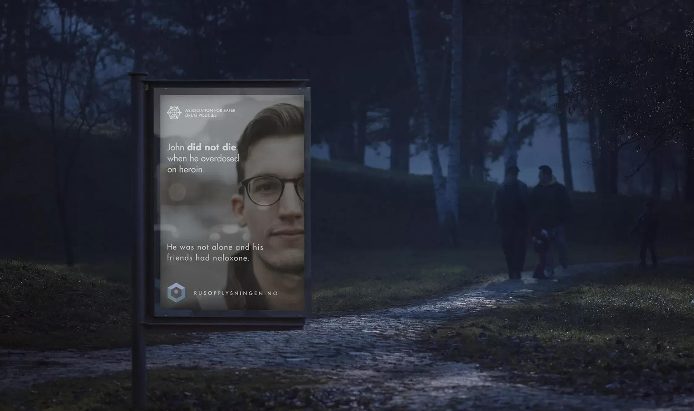 Backlit outdoor ad in a foggy park at night — John did not die when he overdosed, his friends had naloxone.